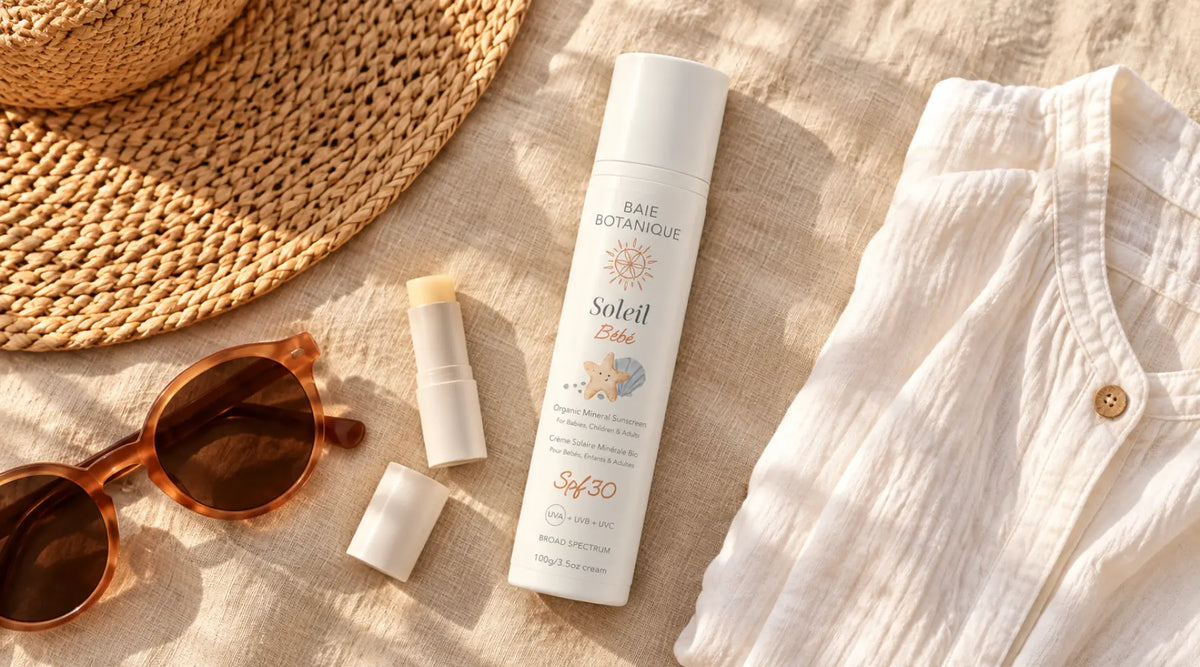 A travel flatlay on warm linen featuring sunscreen, sunglasses, lip SPF, a beach cover-up and a folded map in amber morning light.