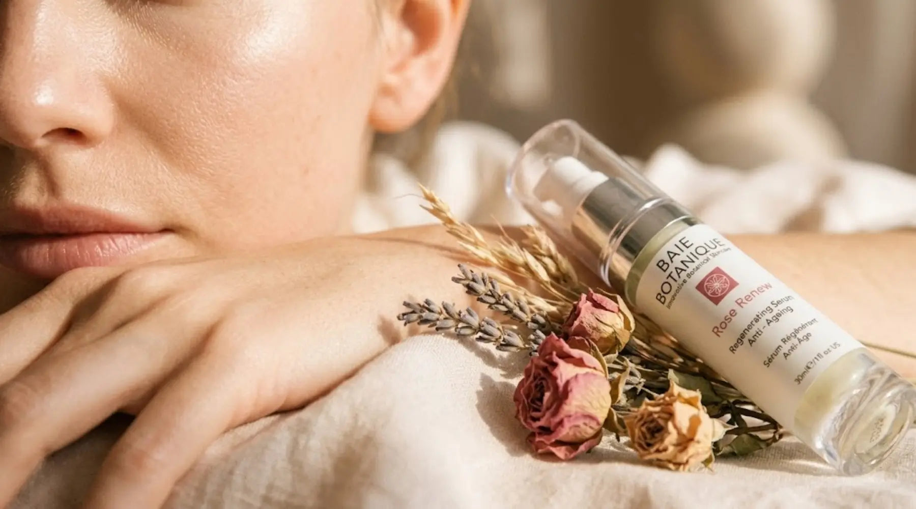 Close-up of calm, luminous skin beside sun-dried botanical flowers on pale warm linen in soft afternoon light