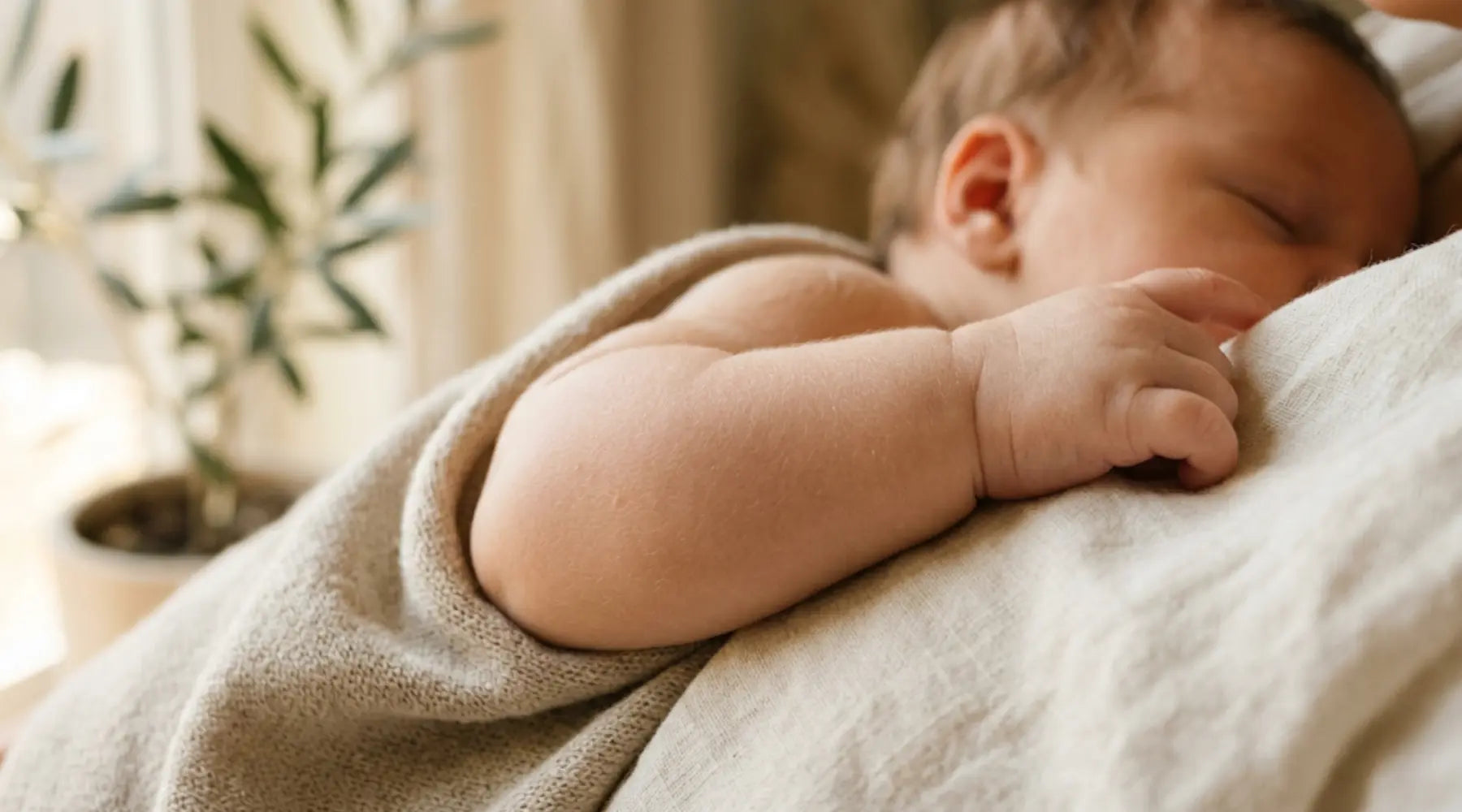 Close-up macro of a baby's soft arm resting on a neutral linen wrap, featuring warm golden light, botanical accents, and a clean skincare editorial aesthetic.