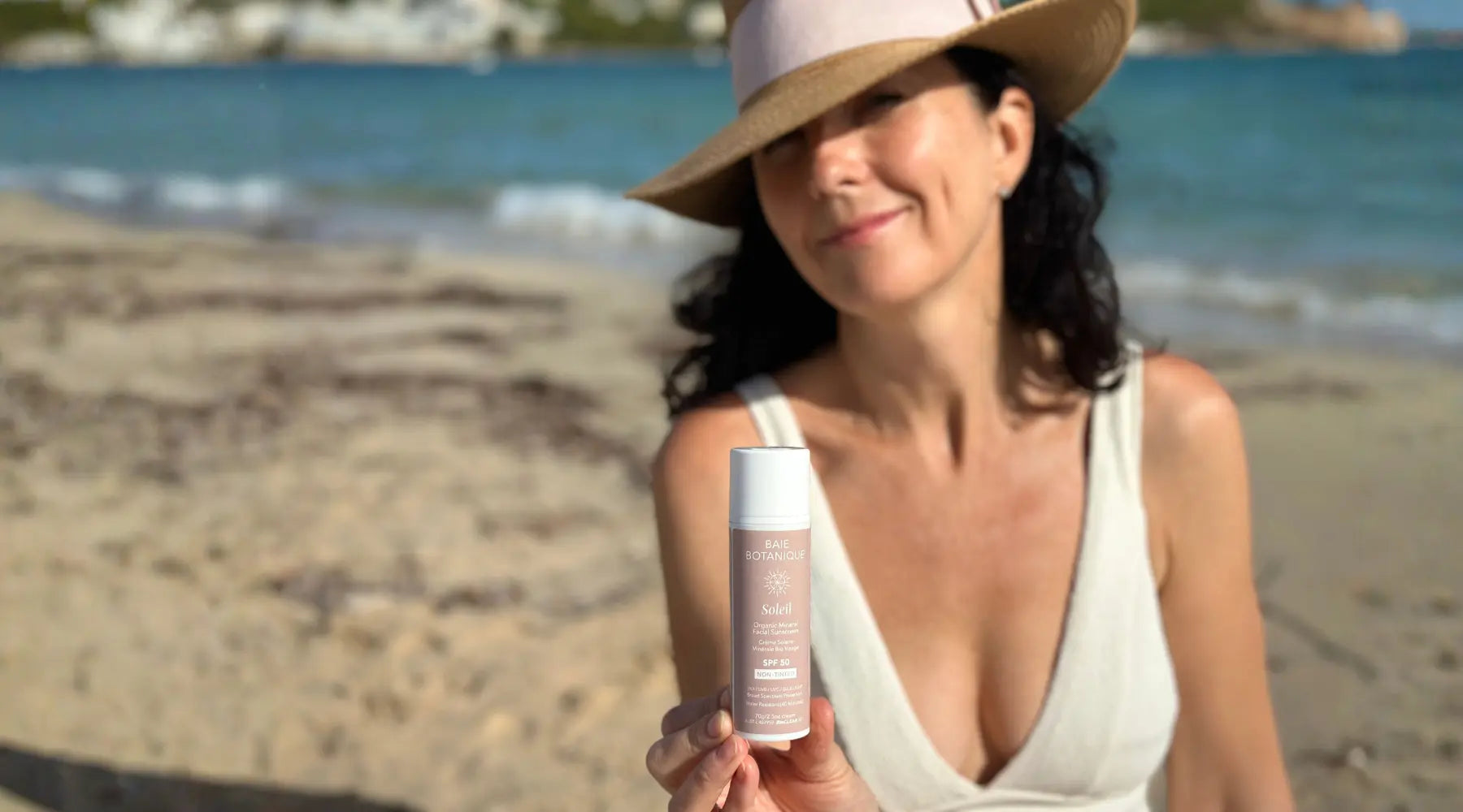 Sophie Oliver holding an organic mineral facial sunscreen SPF 50 in a beach setting