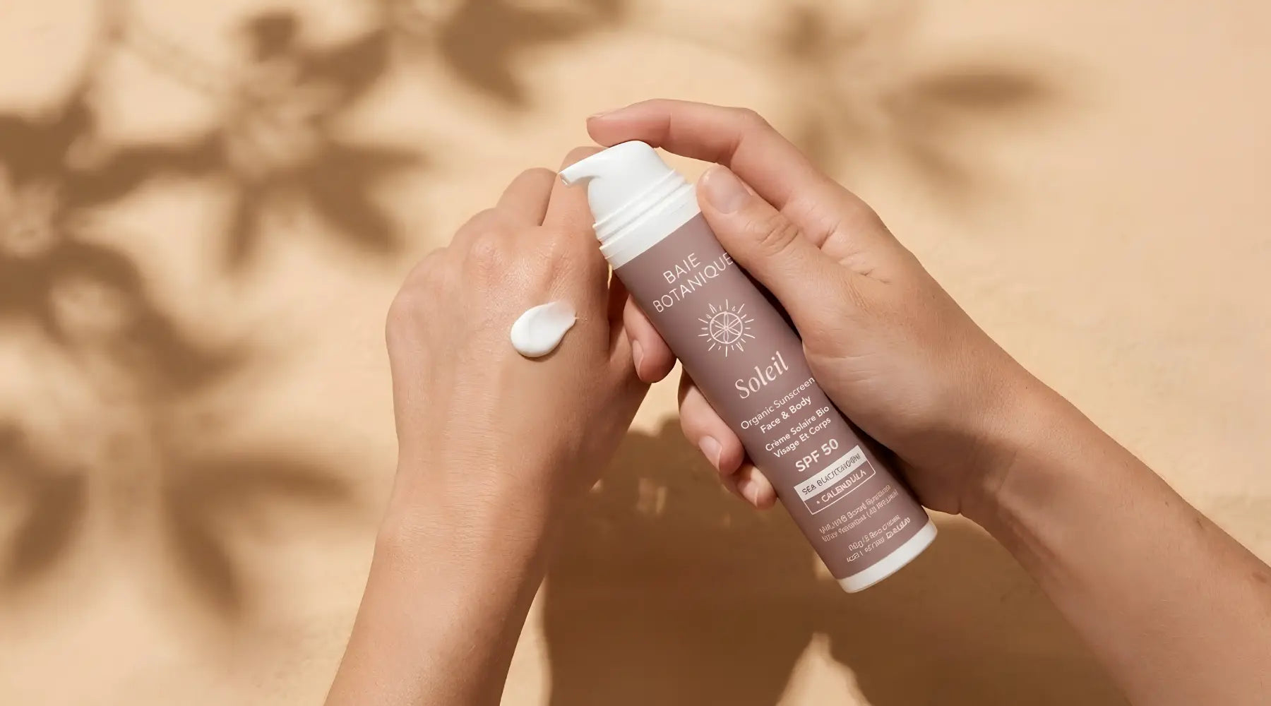A measured amount of Baie Botanique Soleil mineral sunscreen cream dispensed onto a hand, photographed in warm natural light against a sand-coloured surface.
