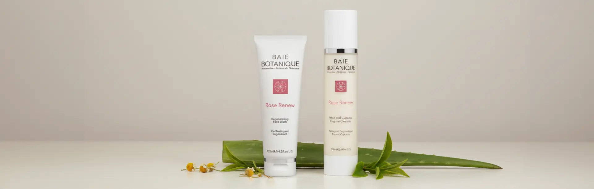 Baie Botanique Rose Renew face wash and enzyme cleanser tubes displayed with chamomile flowers and green leaves on a neutral background.