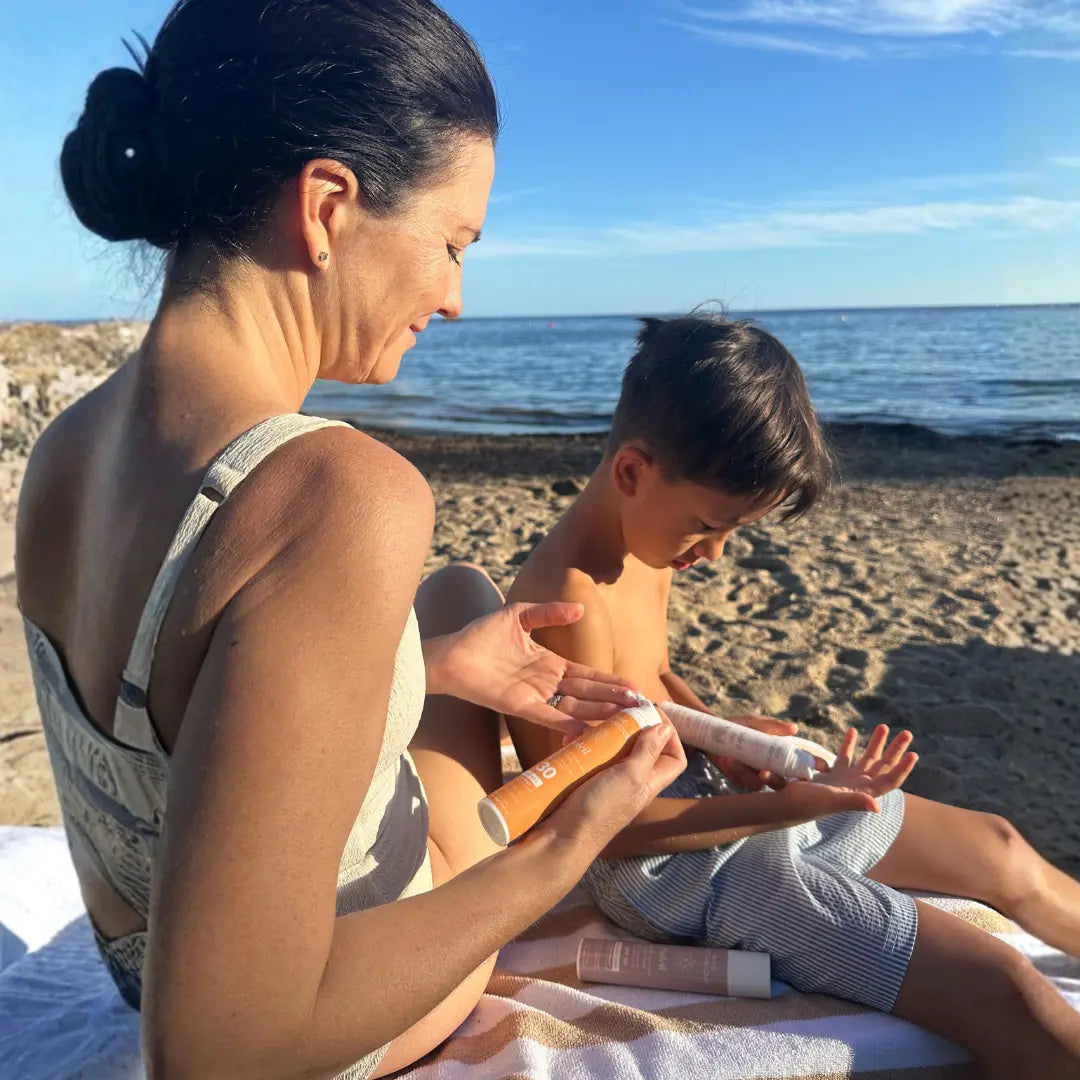 Mother applying mineral sunscreen to child at the beach using natural family sun protection
